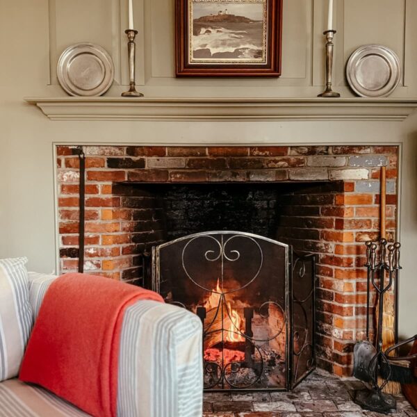 Colonial style fireplace with pewter details and chair with draped pink angora blanket for a Sunday home moment.