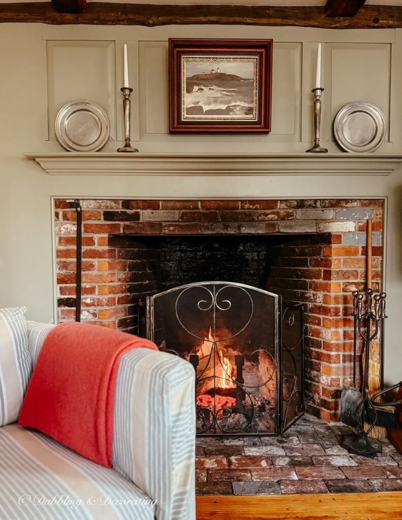 Colonial style fireplace with pewter details and chair with draped pink angora blanket for a Sunday home moment.
