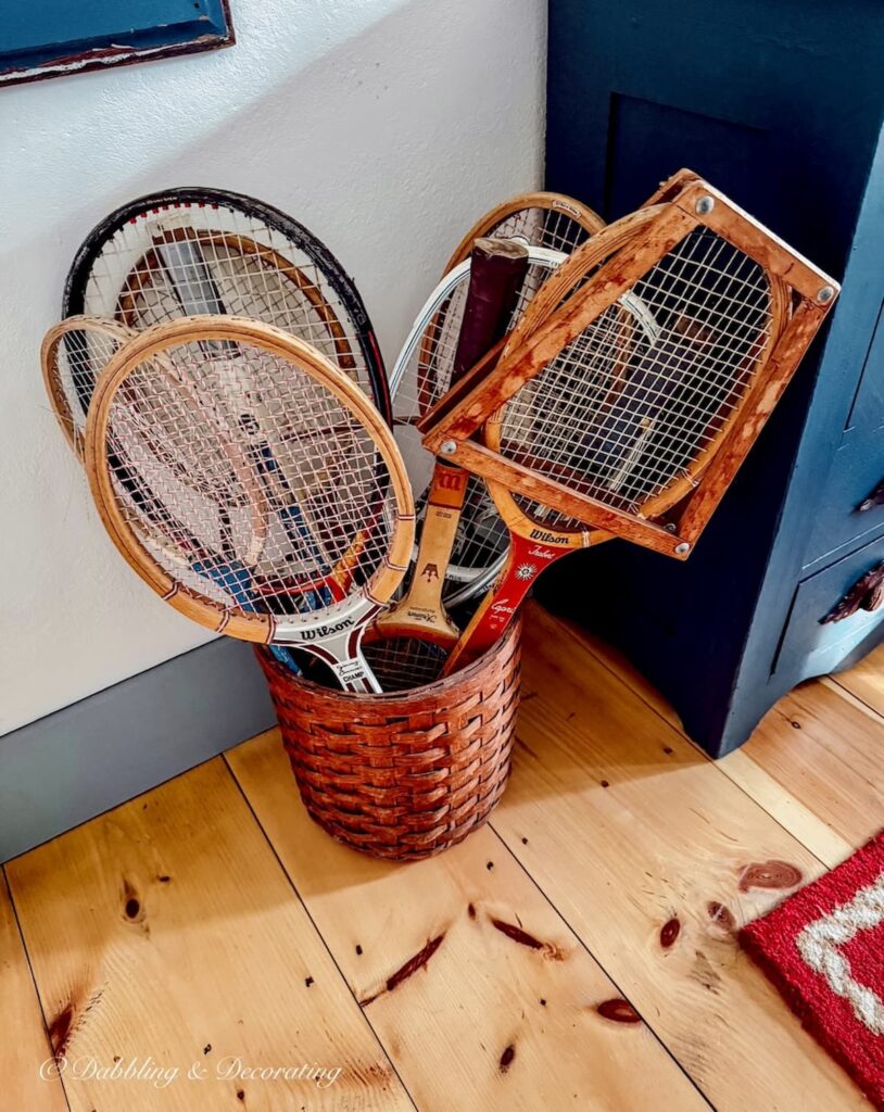 Vintage basket filled with vintage wooden tennis racquets on pine floor in guest bedroom for a Sunday home moment.