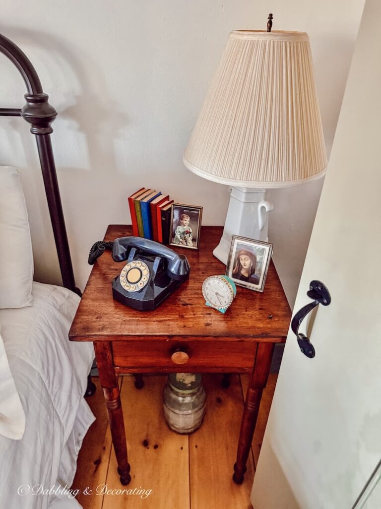 Antique bedside table with old telephone, small bible collection and vintage alarm clock with white lamp.