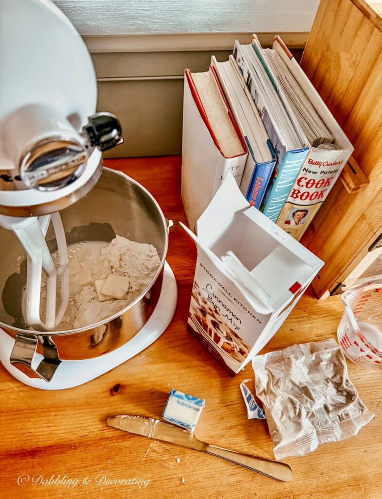 KitchenAid mixer on wooden kitchen countertops with Stonewall Kitchen's Cinnamon bun mix, cookbooks, butter for a Sunday Home Vibe.