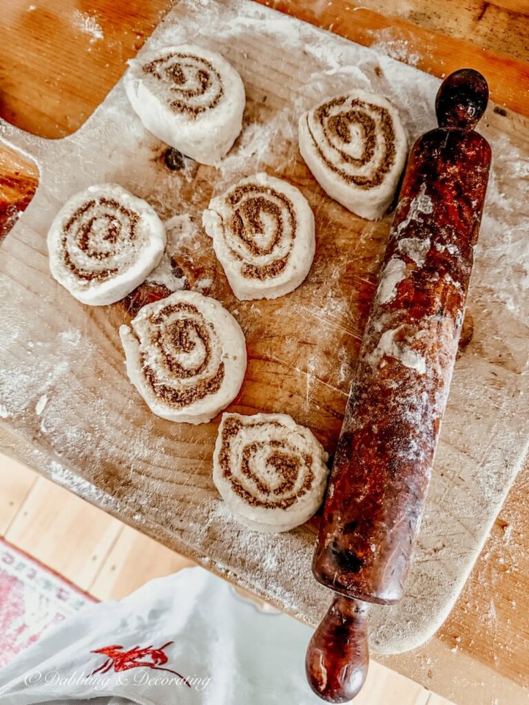 Breadboard with cinnamon bun rolls and antique rolling pin on kitchen counter for a Sunday home moment.