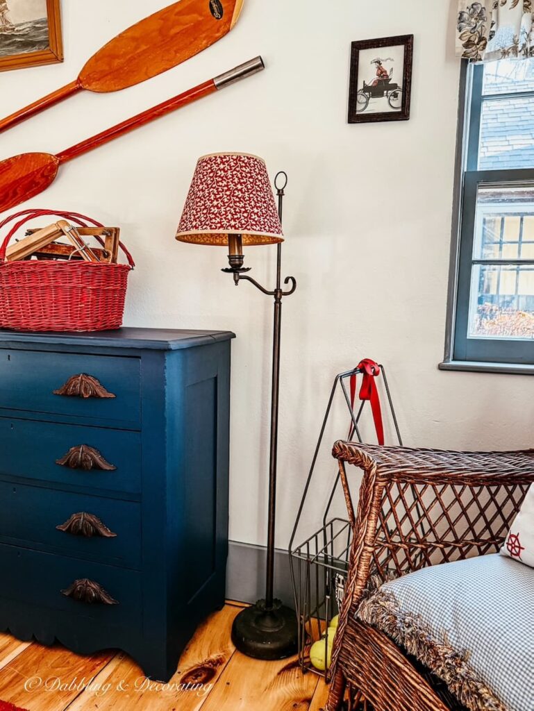 Vintage inspired bedroom with blue dresser, oars on wall, wicker chair and red wrought iron floor lamp for a Sunday home vibe.