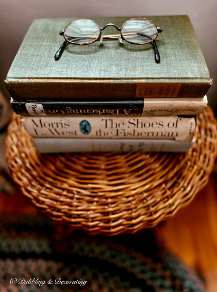 Wicker stool with a stack of books and antique eye glasses styled in a living room corner.