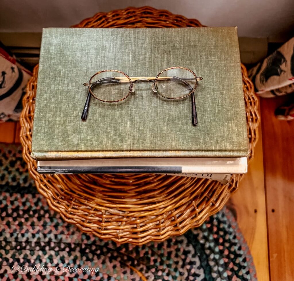 Stack of vintage books with antique eye glasses on stool on braided rug for for a Sunday home decor vibe.