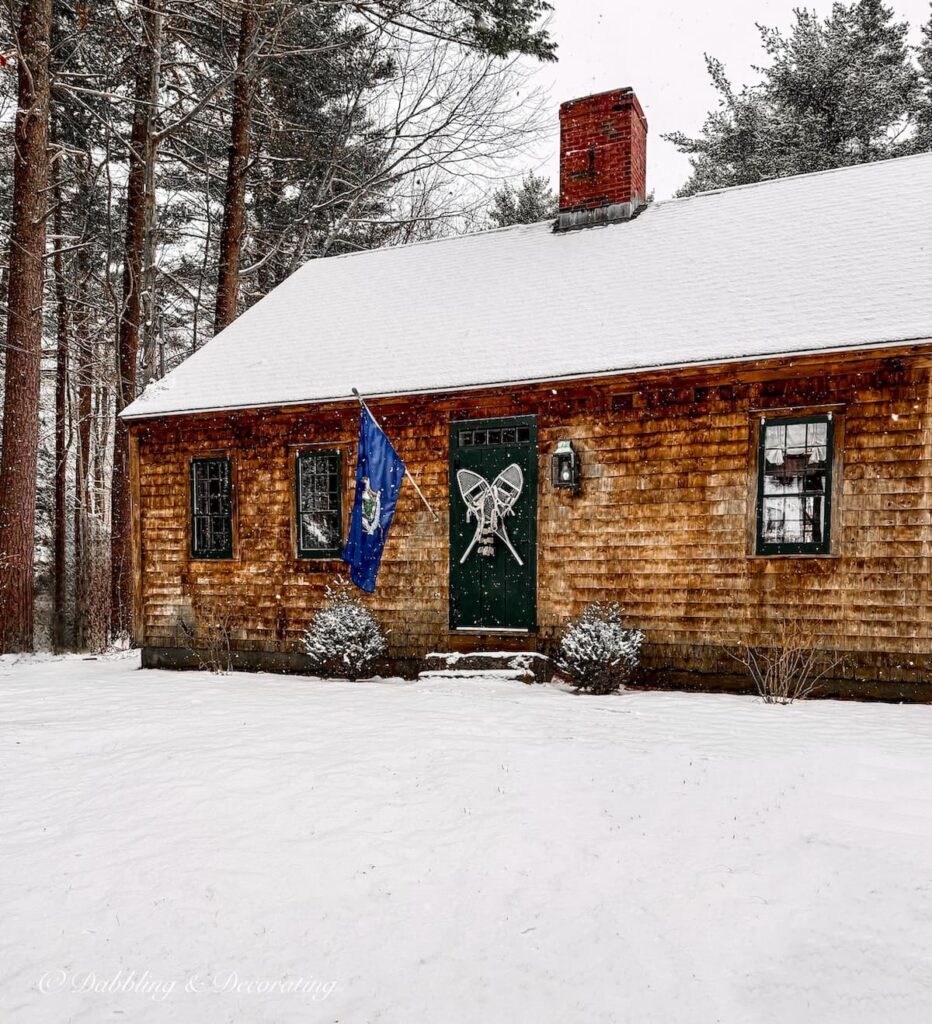 Early American Cedar shakes home in the snow with Maine flag and vintage white snowshoes on Essex Green styled front door on a snow day