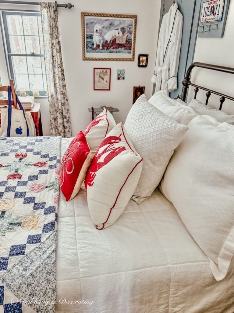 Small guest bedroom with quilted bedding on wrought iron bed with coastal details like lobster pillows at home in Maine.