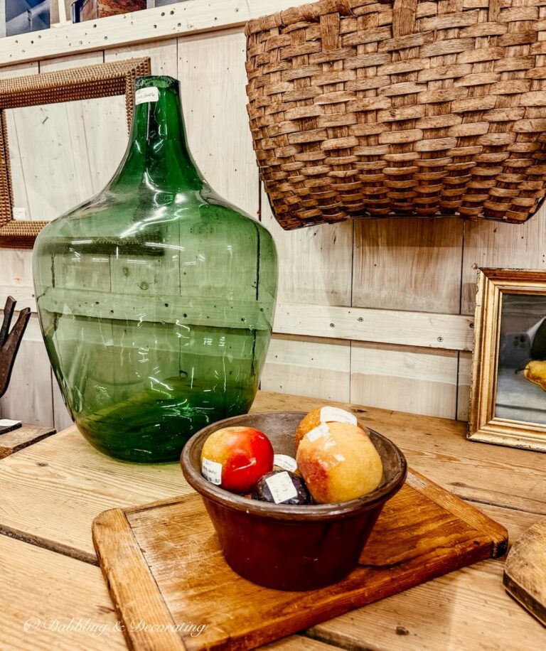 Antique green bottle highlighted on antique store table with a bowl of fruit and a breadboard and basket for St. Patrick's Day decor ideas.