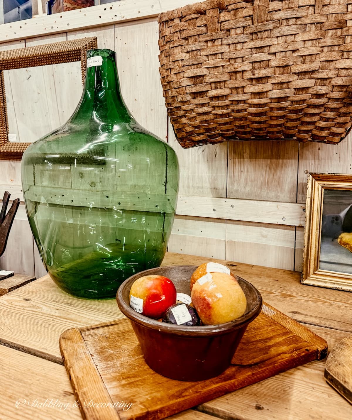 Antique green bottle highlighted on antique store table with a bowl of fruit and a breadboard and basket for St. Patrick's Day decor ideas.