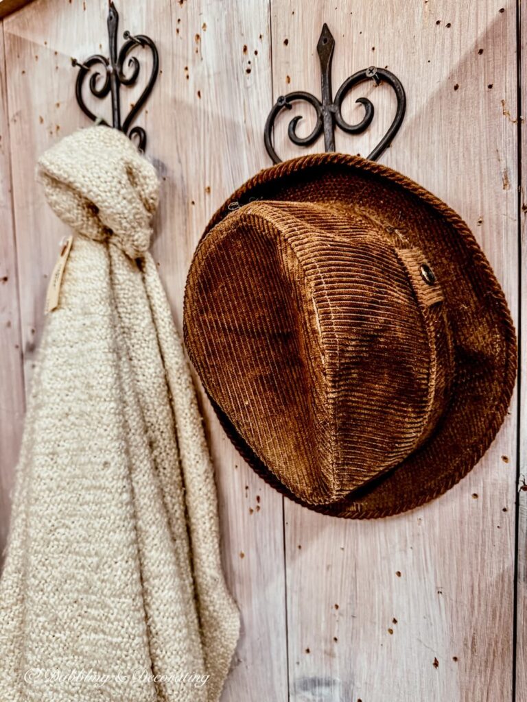 Corduroy brown hat on heart wrought iron wall rack with Irish white blanket for St. Patrick's Day Decor in antique store.
