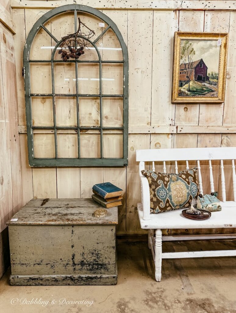 Vintage salvaged green window on wall above green trunk with white bench in antique store for St. Patrick's Day decor ideas.