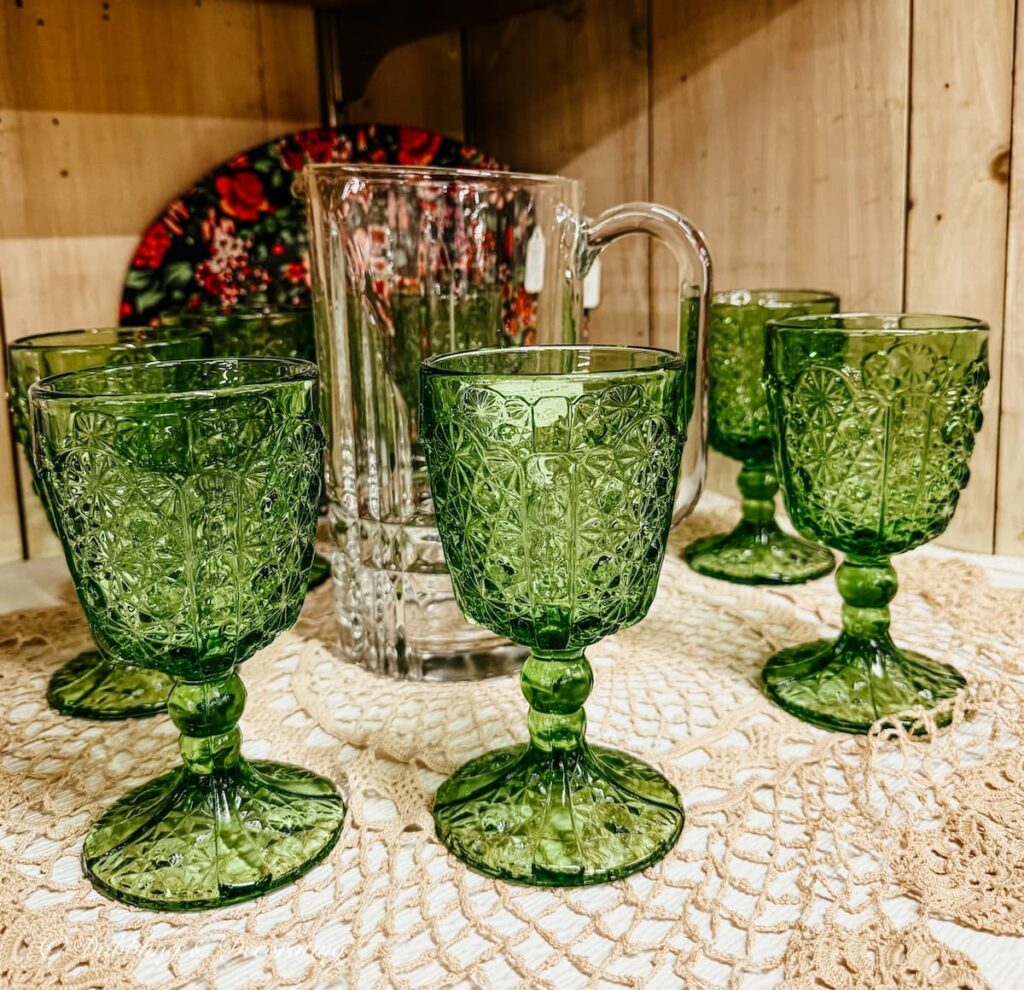 Vintage green glasses surrounding glass pitcher on shelf in antique store for St. Patrick's Day decor ideas.