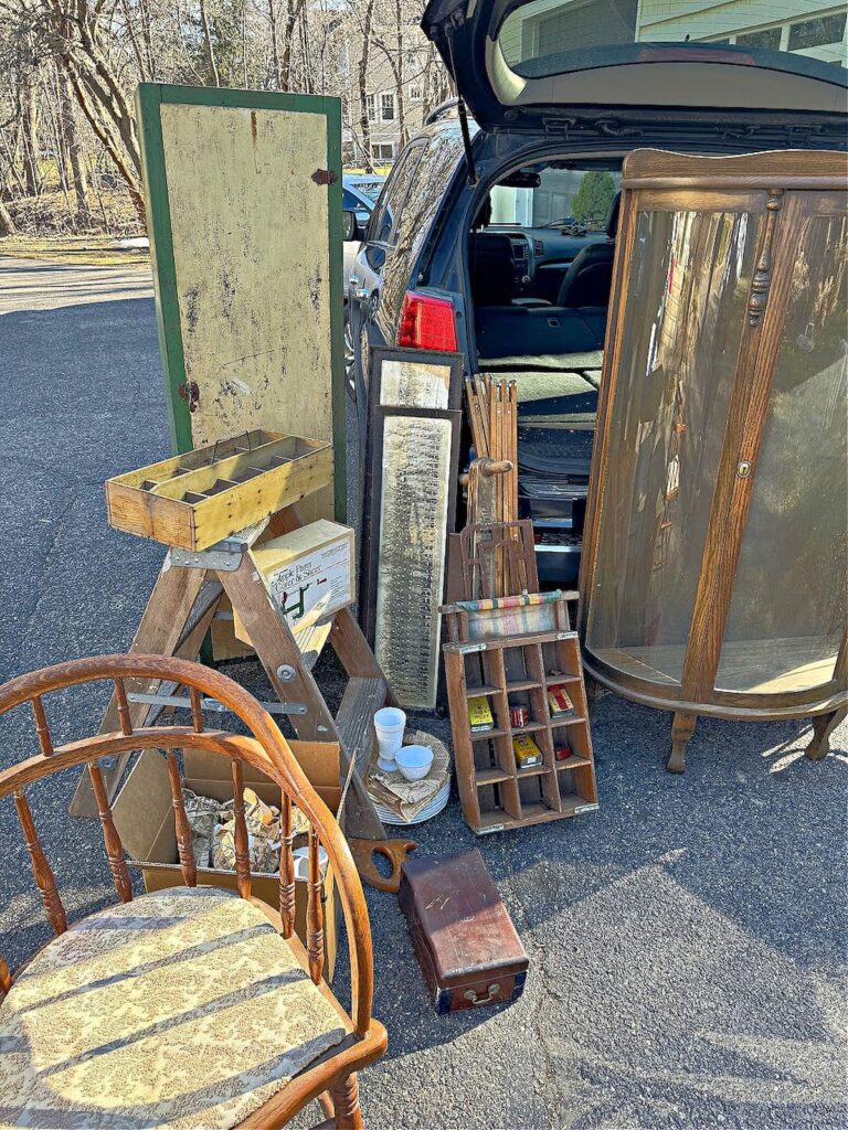 Vintage haul outside of a car with chair, cabinet, crates, and more.