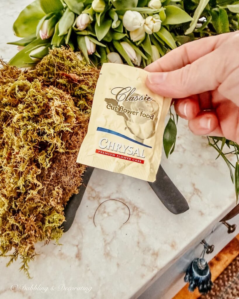 Plant food in small packet in hand to add to Vintage Wooden Bucket Flower Arrangement.