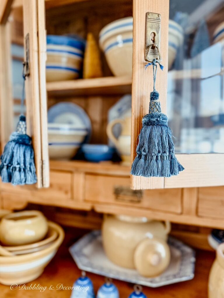 Small vintage decor ideas using blue tassels on a pine hutch for a cozy eclectic vibe.