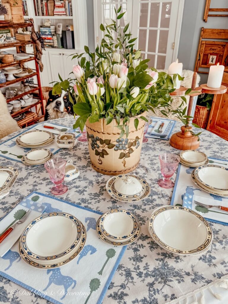 Vintage wooden bucket flower arrangement with white and pale pink tulips on table setting centerpiece with dog peaking on.