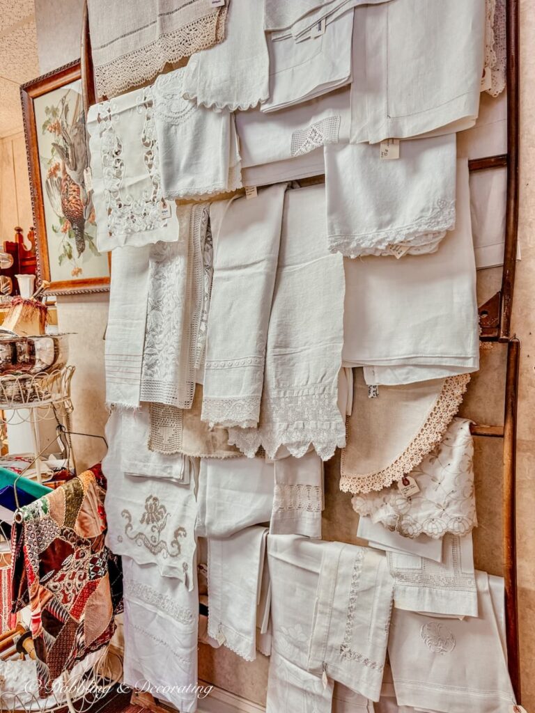 Collection of white Irish linens hanging on the wall in an antique store.