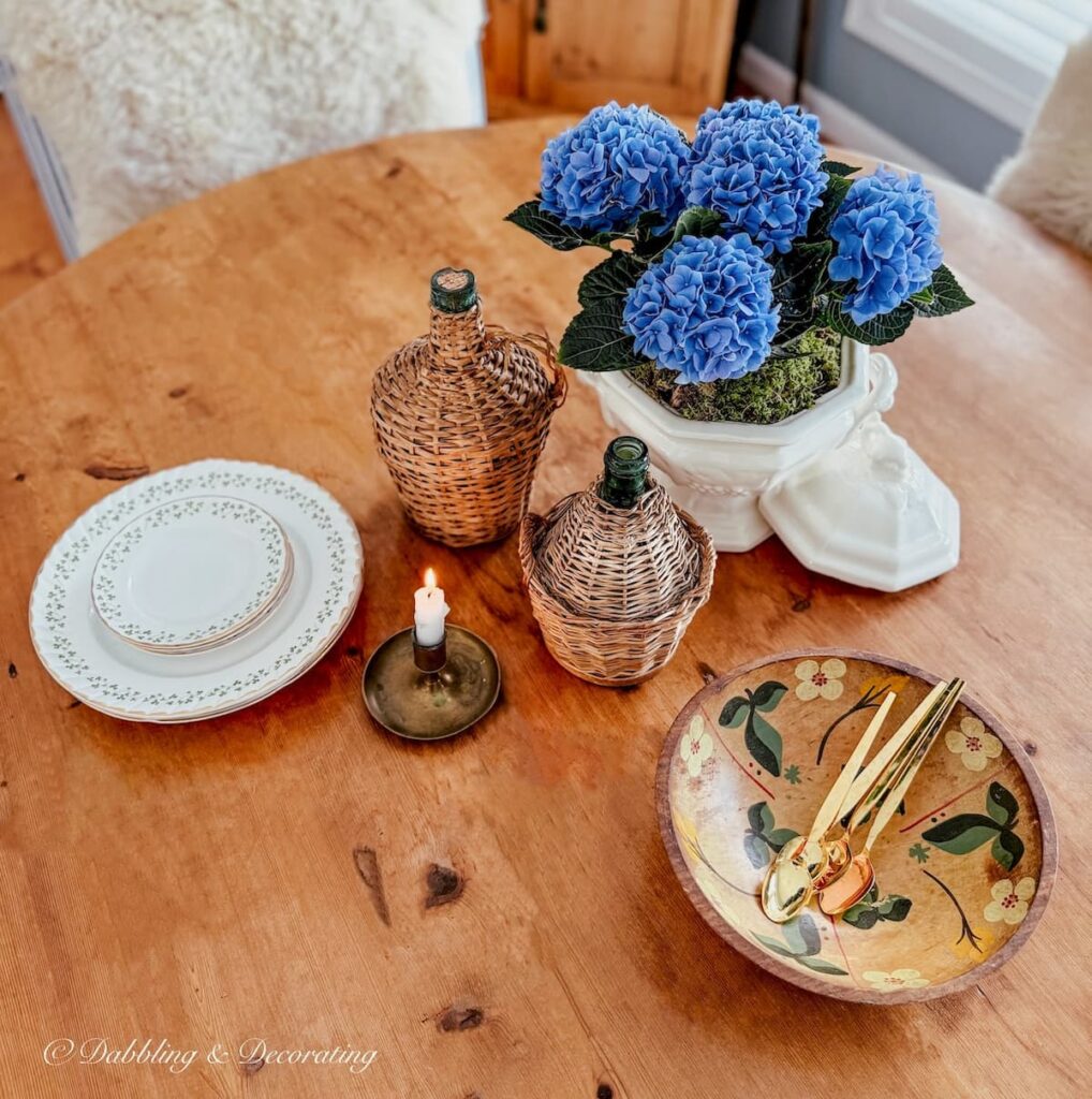 Vintage soup tureen with blue hydrangeas, vintage wooden bowl, demijohns candle and Irish dishes vintage small decor ideas on antique pine table.