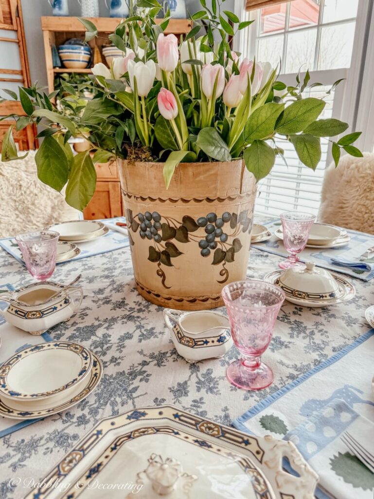 Vintage wooden bucket flower arrangement with old painted maple sap bucket from New England on table with pink and white tulips.