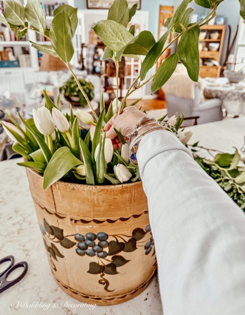 Vintage wooden bucket flower arrangement being arranged by hand with white tulips and greenery.