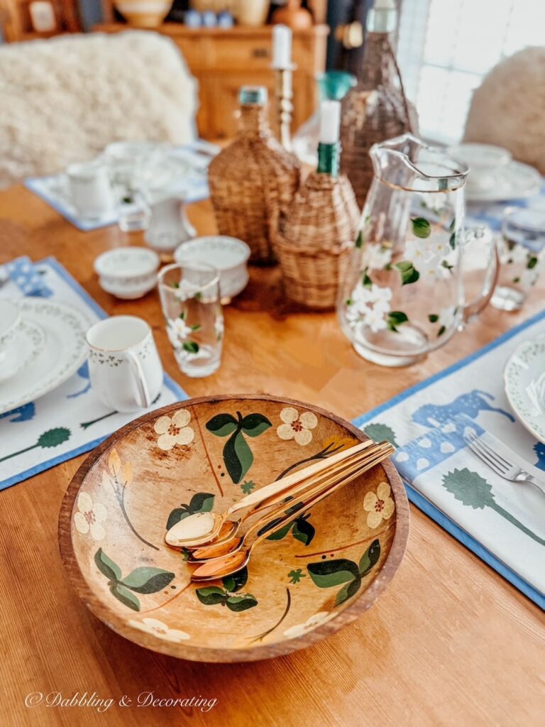 Wooden bowl painted with green leaves on table with gold dessert spoons for small vintage decor ideas.