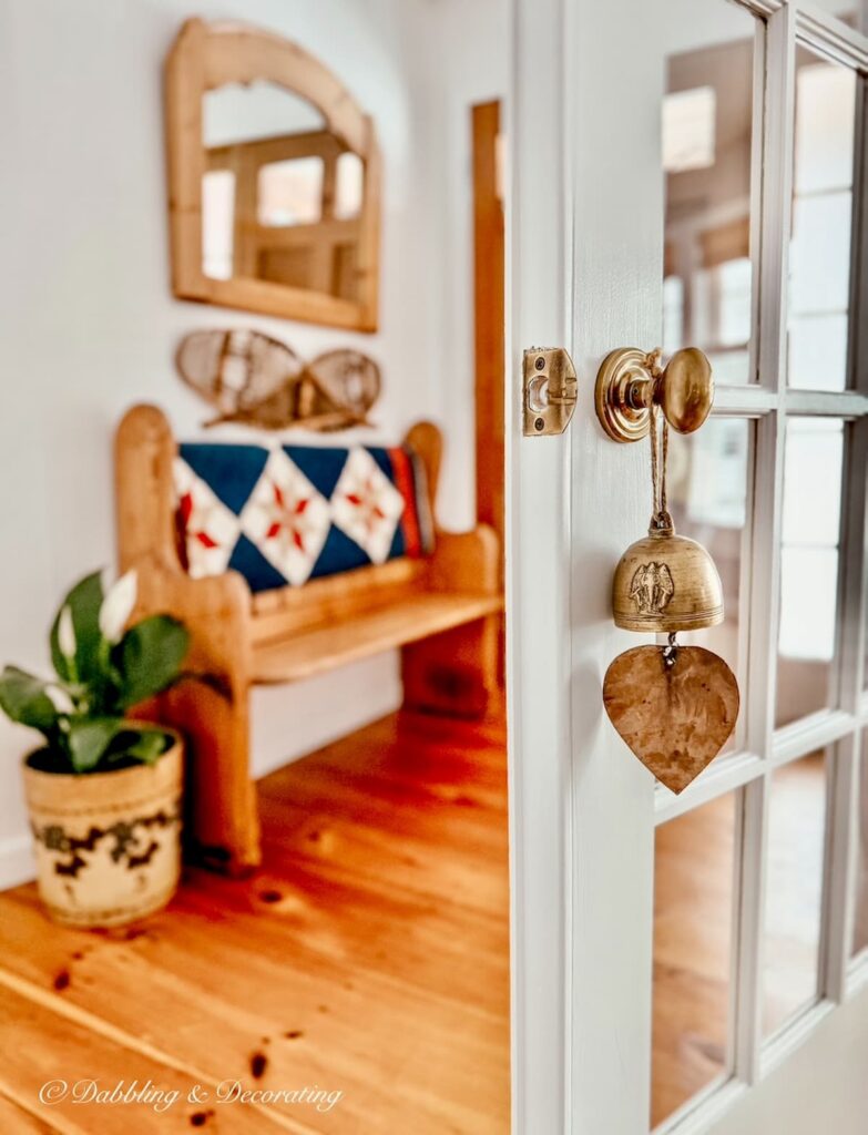small vintage decor ideas with a vintage brass bell hanging on white French door knob into winter styled entryway with vintage church pew bench.
