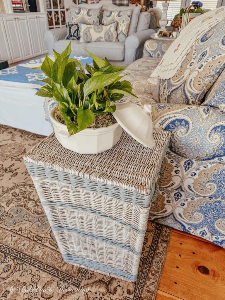 Vintage inspired blue and white styled living room with wicker basket side table and thrifted white soup tureen with green plants on display.