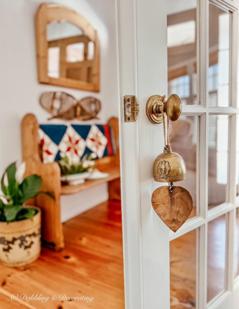 Vintage inspired entryway with wood floors, vintage church pew and antique bell on open French door and thrifted soup tureen planter ideas on bench.