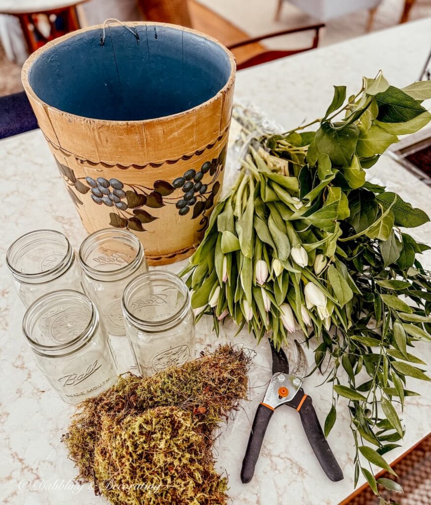 Materials needed to create a vintage wooden bucket flower arrangement with white tulips and a vintage maple sap bucket with mason jars for water and moss.