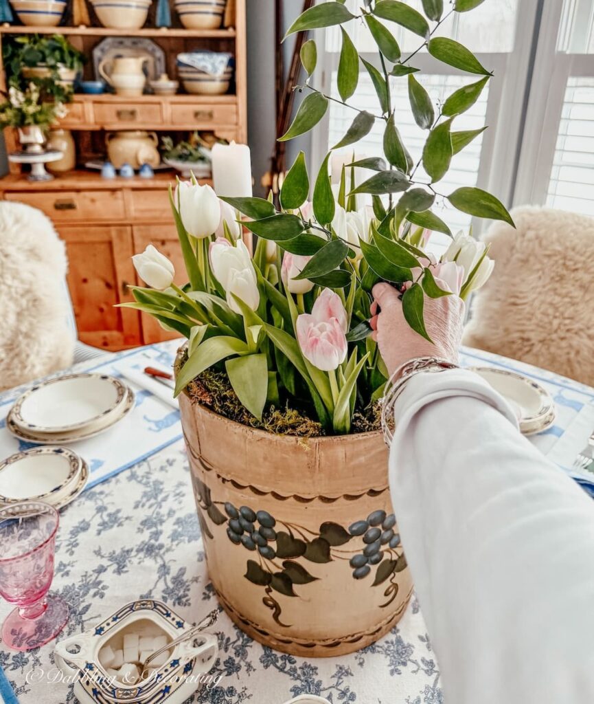 Vintage wooden bucket flower arrangement with maple sap bucket, white tulips, and hand adding greenery to this spring centerpiece.
