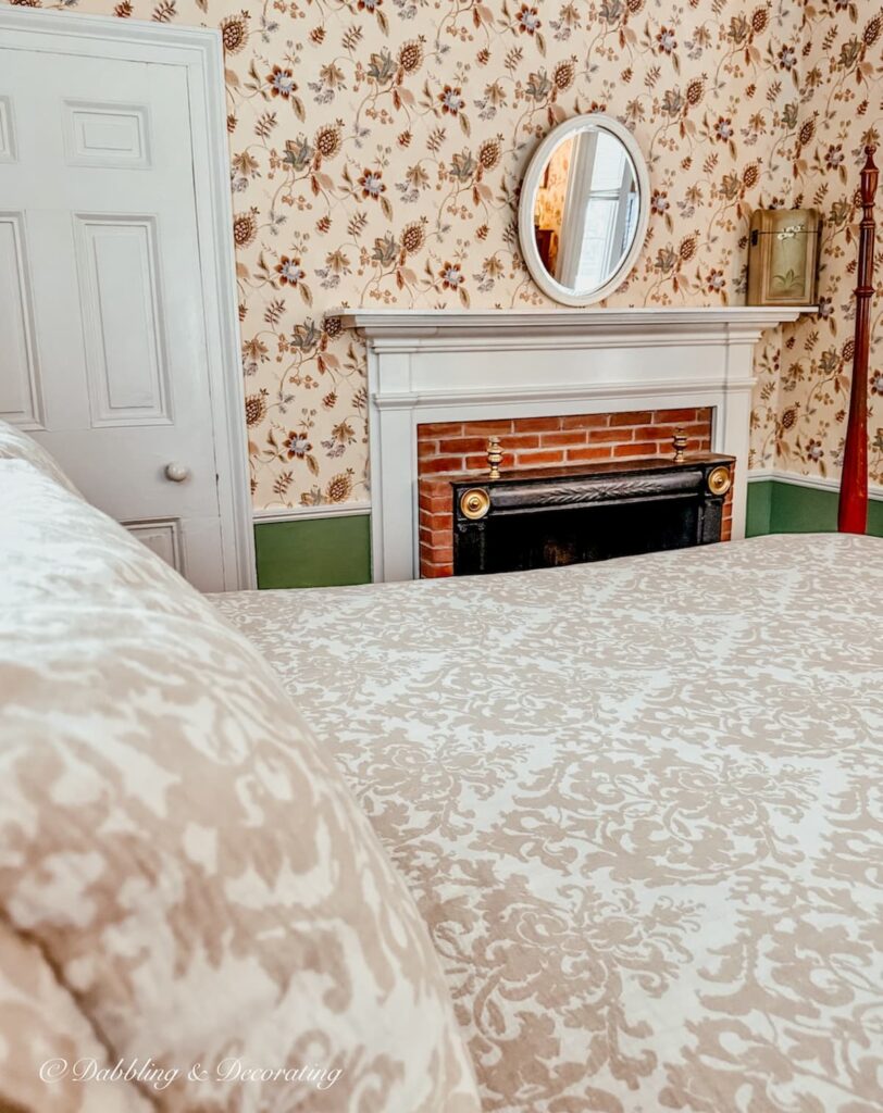 Bedroom wallpaper ideas at the Quechee Inn in Vermont with tan and white patterned bedding paired with wallpaper and antique fireplace.