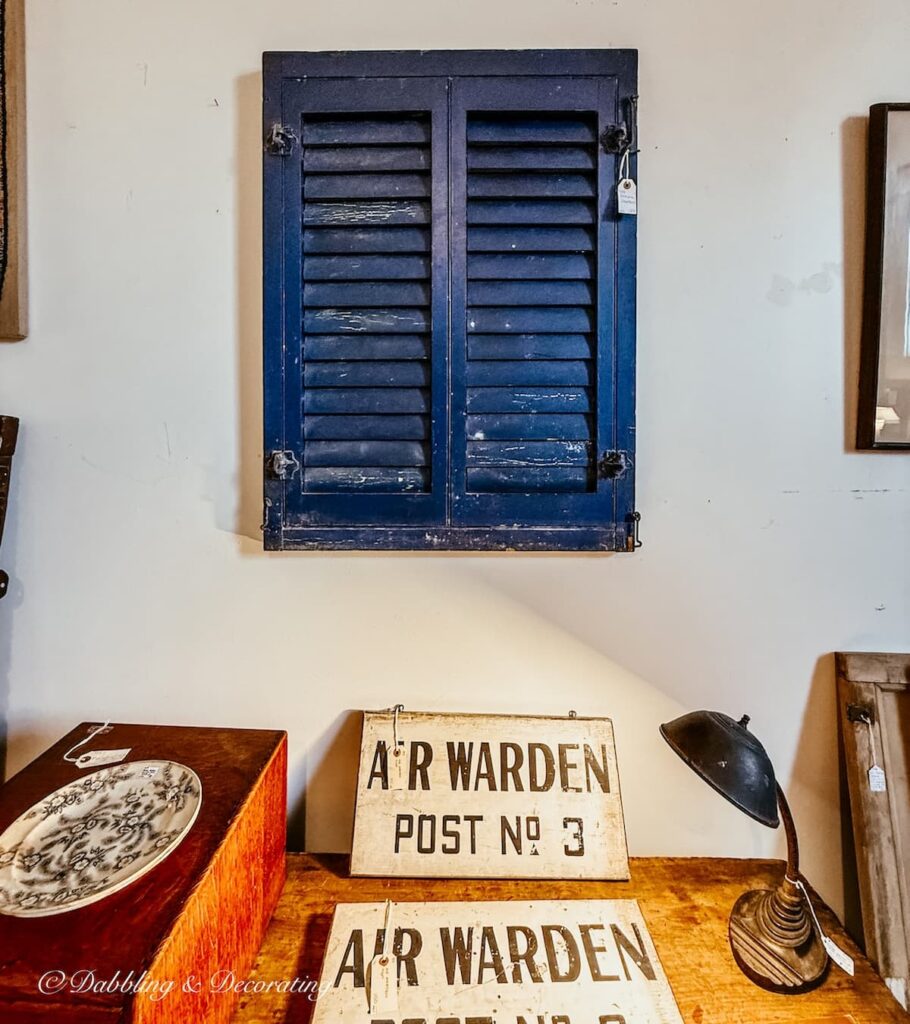 A pair of blue shutters hanging on an antique store wall over a desk with eclectic home decor ideas.
