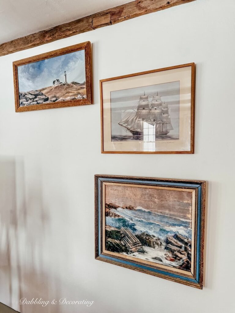 The start of a coastal inspired gallery wall with lighthouse, sailboat and rocky coast paintings in Maine home.