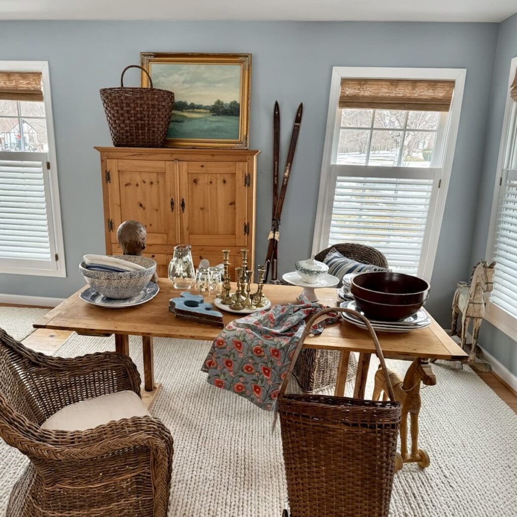 Open floor plan Scullery-Inspired Kitchen Workroom with pine hutch and table with wicker chairs and white rug.