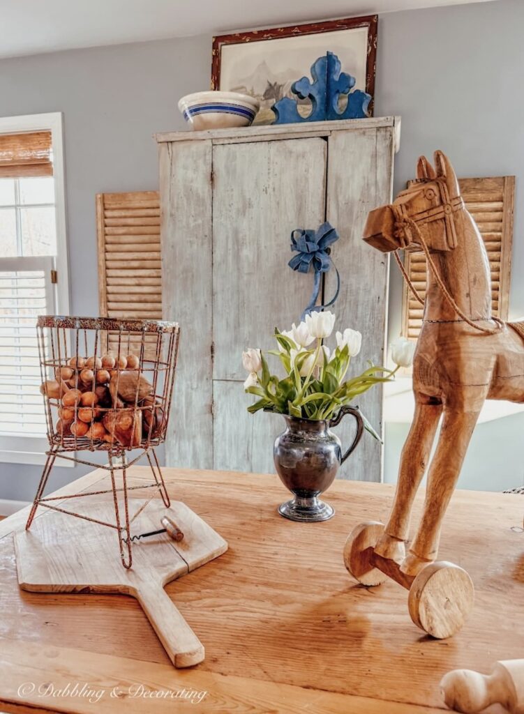 Tall blue Antique cupboard on wall with layered wooden table and vintage finds in kitchen scullery-inspired workroom.