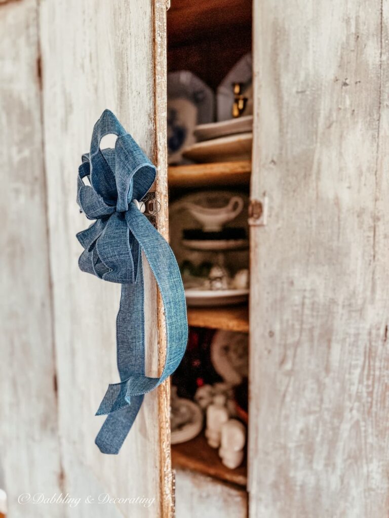 Antique cupboard ideas in a blue hutch with an open door and a sneak peak at dishes inside and blue bow on open door handle.