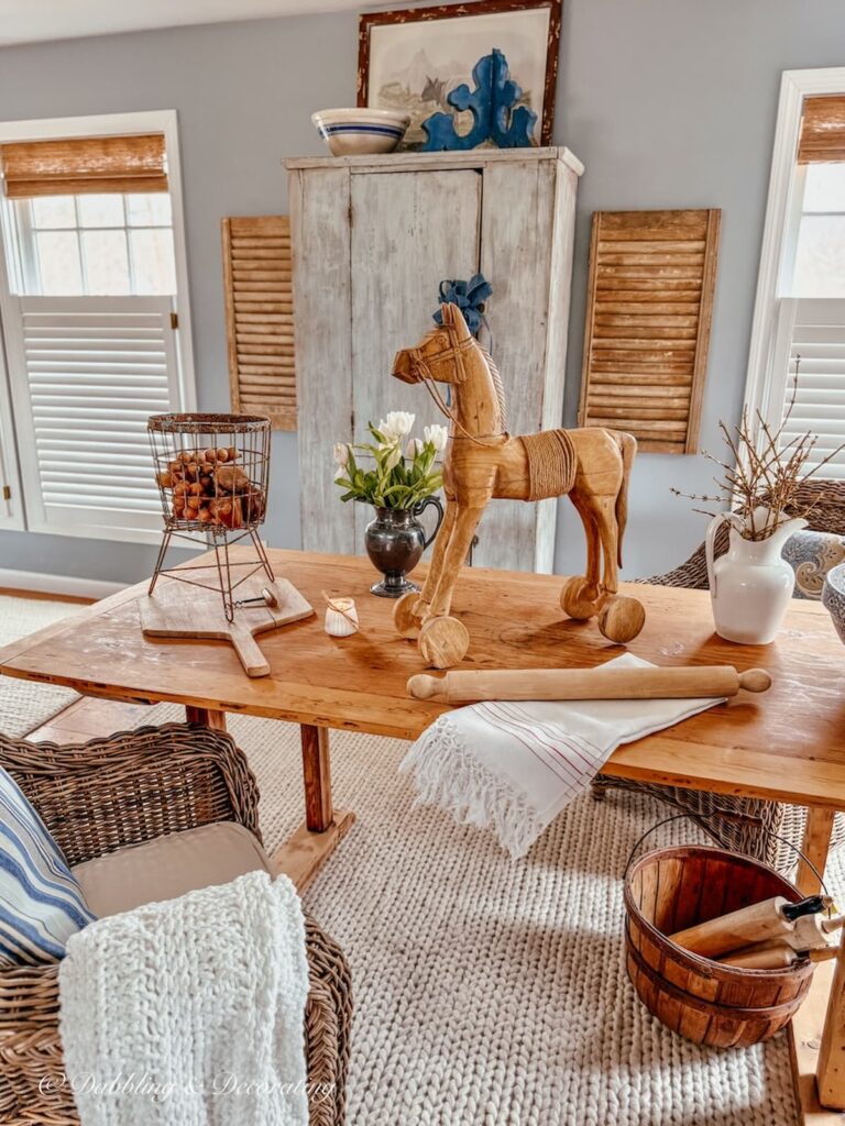 Vintage styled room in open floor plan with large pine table, vintage finds and a blue antique cupboard on wall styled with vintage finds.