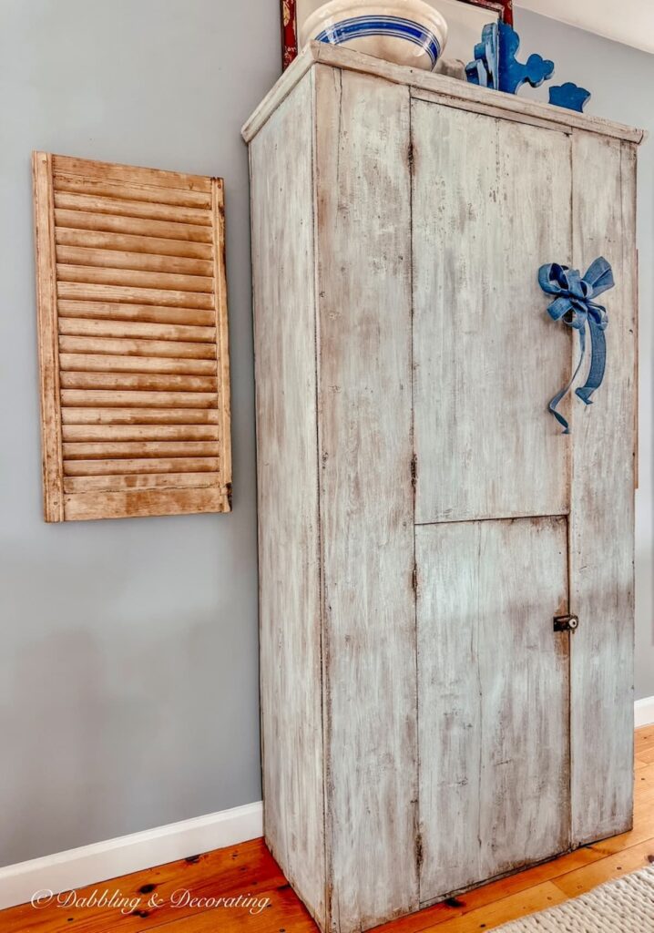 Antique cupboard ideas with a blue hutch with closed vintage storage against open floor plan blue wall with wooden shutter.