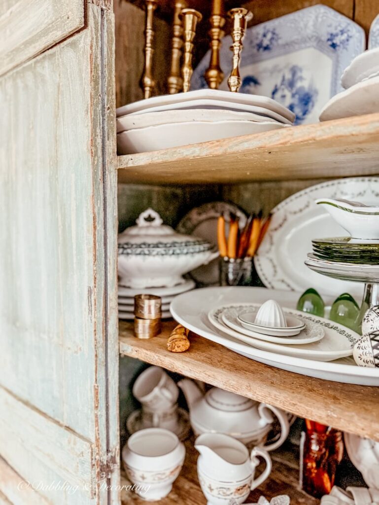 Antique cupboard ideas with open door and view into the vintage dishes stacked and layered on shelves.