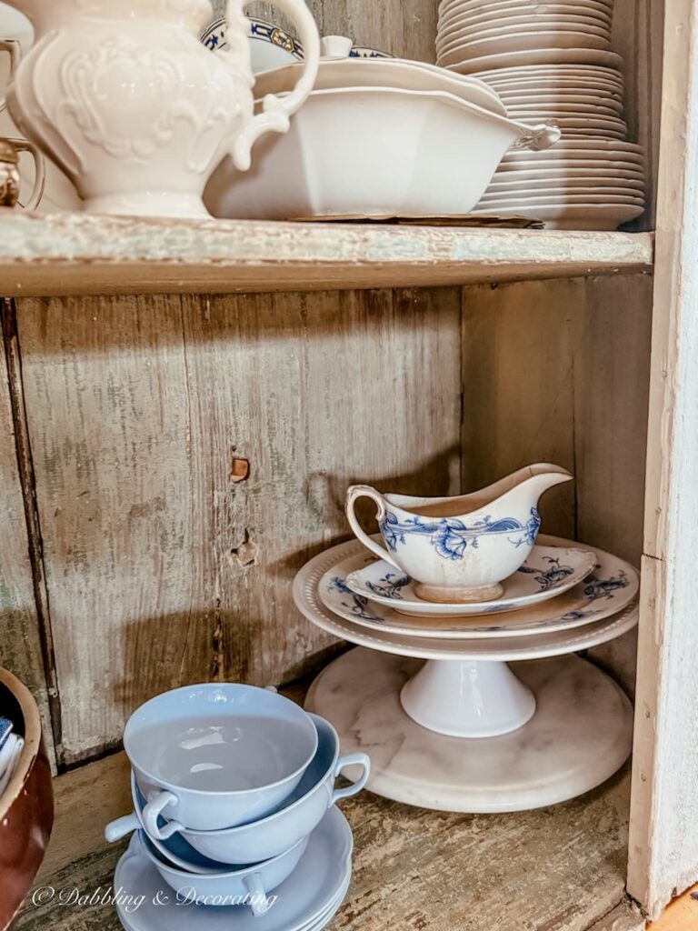 Antique hutch shelves with vintage dishes stacked and layered by colors like blue and white.