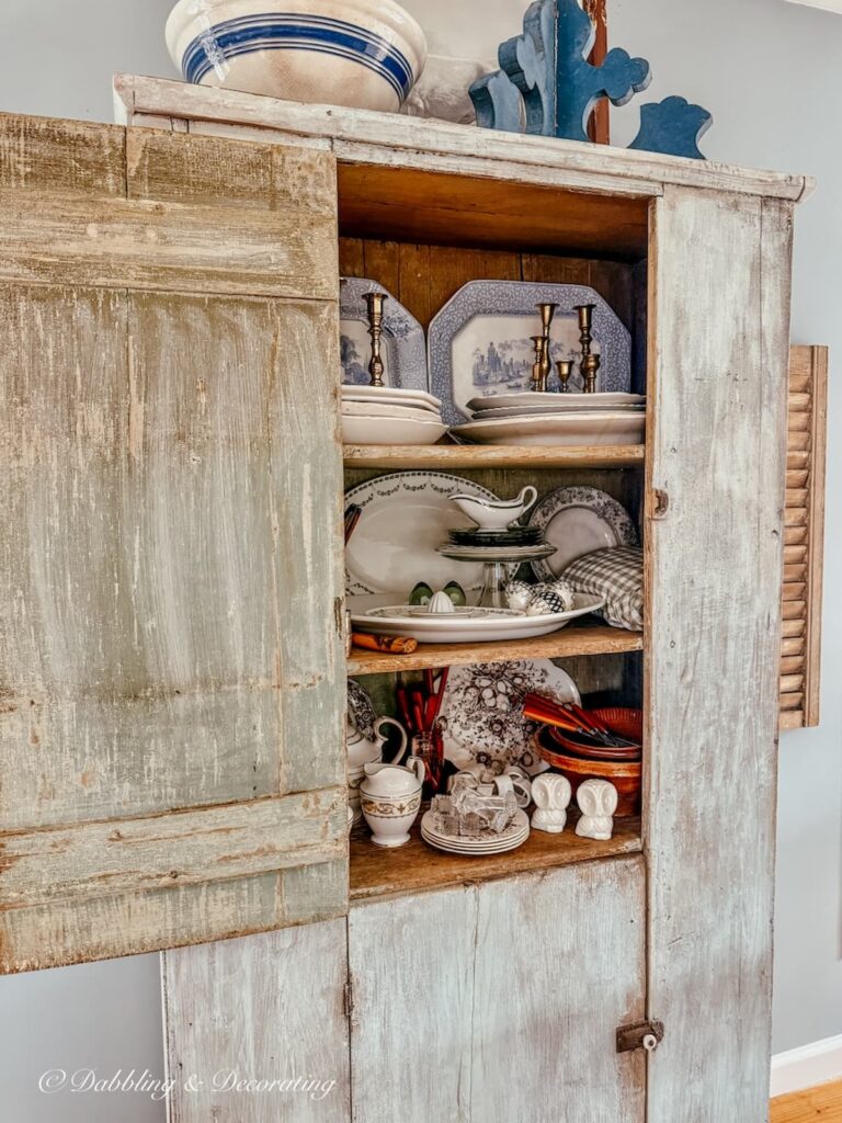 Antique cupboard in scullery-inspired open floor plan workroom with open top door for vintage decor storage.