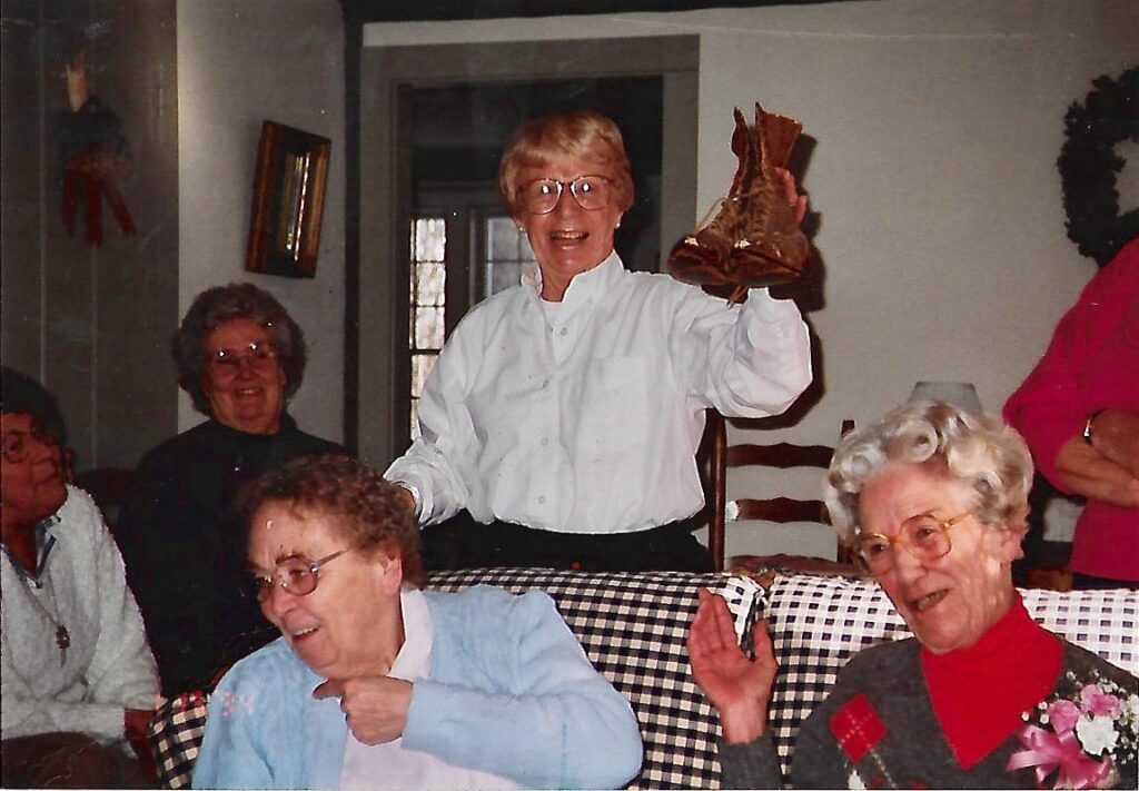 My mother after a day antiquing with her friends holding up a pair of antique boots gathered in the dining room with her friends.