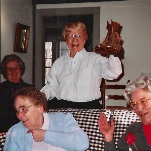 My mother after a day antiquing with her friends holding up a pair of antique boots gathered in the dining room with her friends.