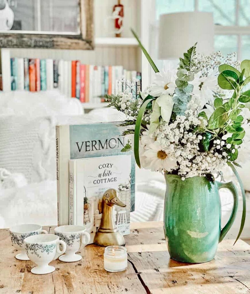 Green pitcher of spring flowers and Vermont book on coffee table for thrifted spring decor ideas.