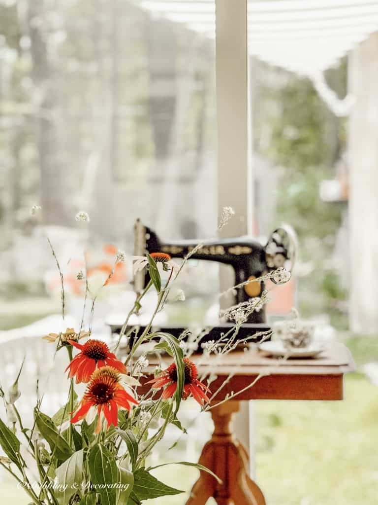 Old sewing machine; black Singer on thrifted wooden table with flowers in sunroom.