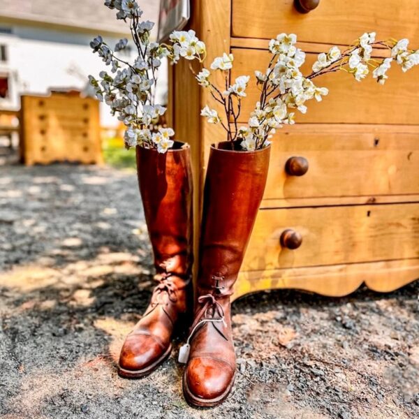 Vintage women's leather boots with spring flowers next to antique dresser outdoors for early spring decor ideas.