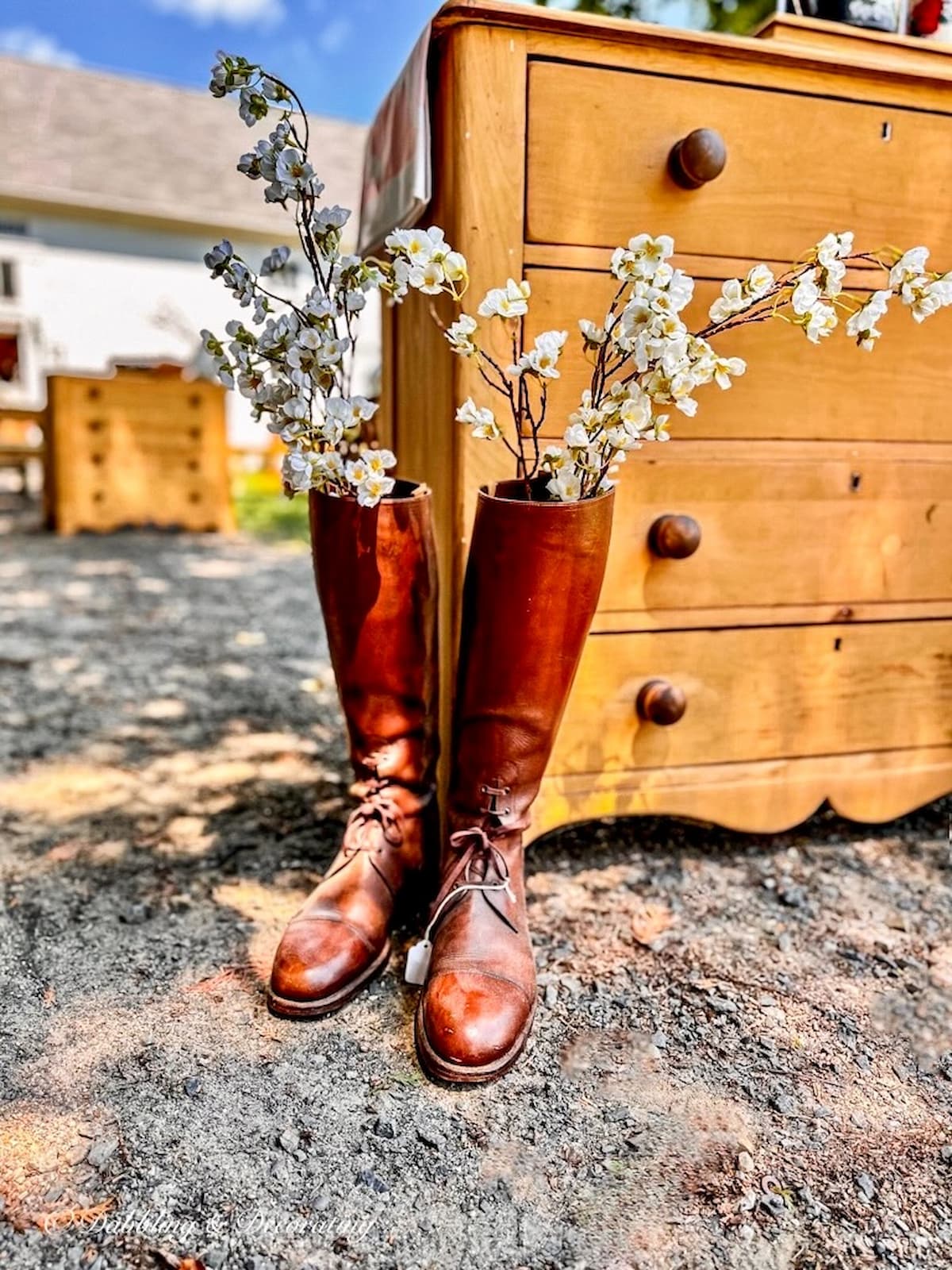 Vintage women's leather boots with spring flowers next to antique dresser outdoors for early spring decor ideas.