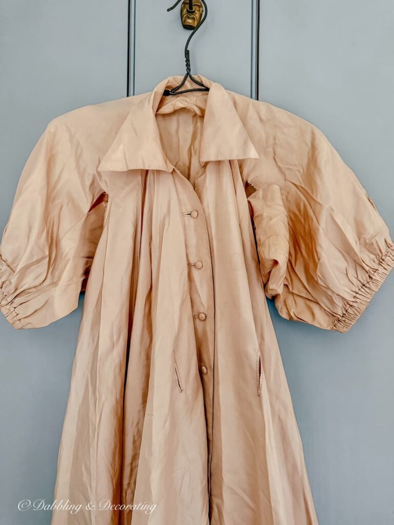 Thrifted beige antique taffeta gown hanging on vintage clothes hanger on bedroom door for thrifted bougie decor ideas.