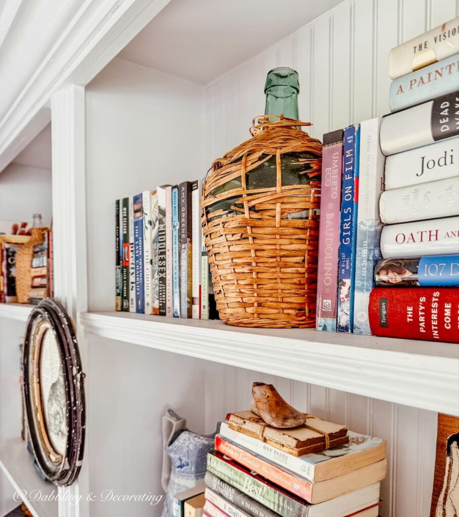White built-in bookshelves filled with books and a vintage demijohn breaking up the spacing in eclectic home decorating ideas.