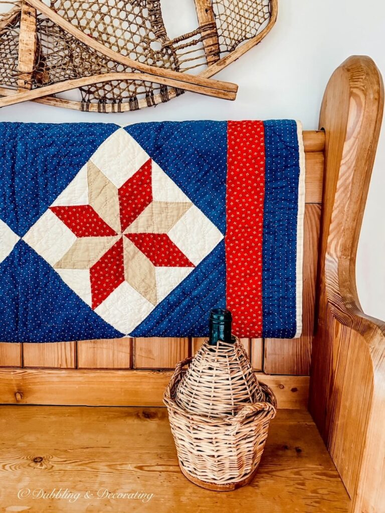 Vintage pine church pew in entryway with blue and red quilt, one vintage demijohn and snowshoes on wall in eclectic home decor ideas.